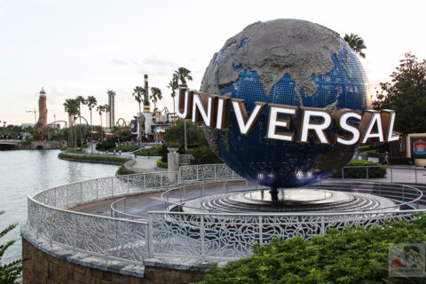 The large rotating Universal globe on its fountain plinth beside the lagoon at Universal Orlando, with palm trees and a lighthouse in the distance