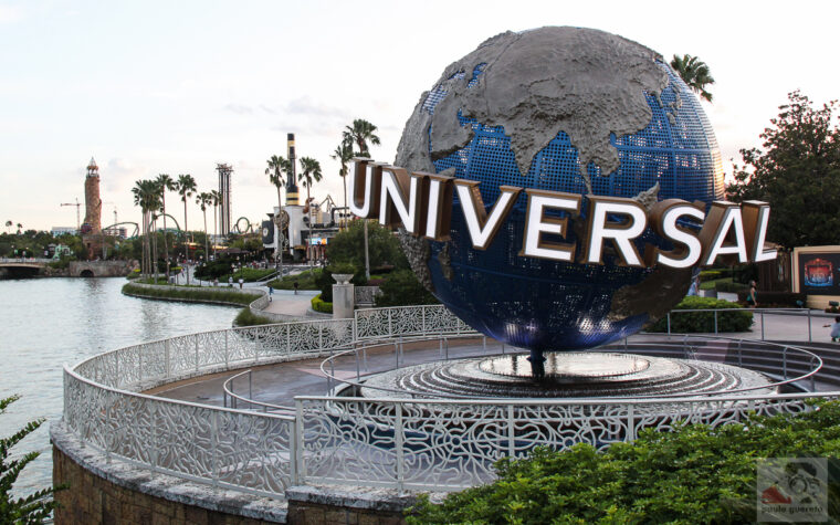 The large rotating Universal globe on its fountain plinth beside the lagoon at Universal Orlando, with palm trees and a lighthouse in the distance