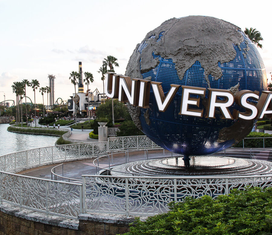 The large rotating Universal globe on its fountain plinth beside the lagoon at Universal Orlando, with palm trees and a lighthouse in the distance